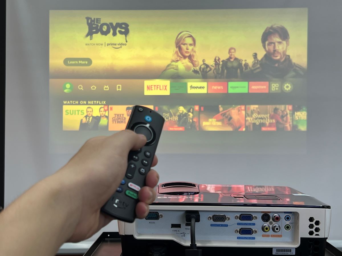 A hand is holding the fire stick remote with the Epson projector projecting on the screen