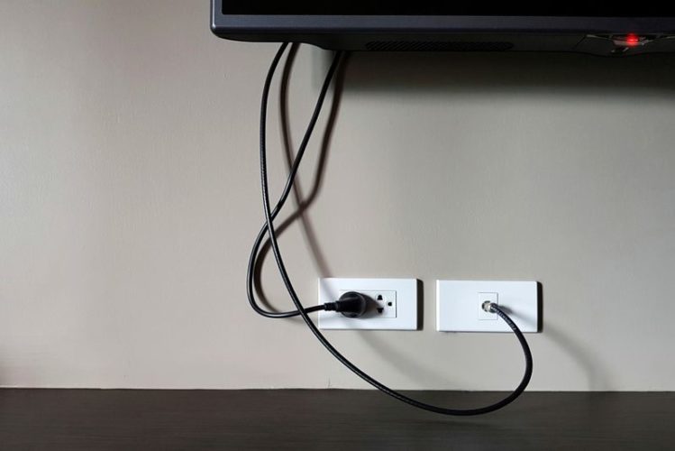 a black TV plugged into a wall electrical socket