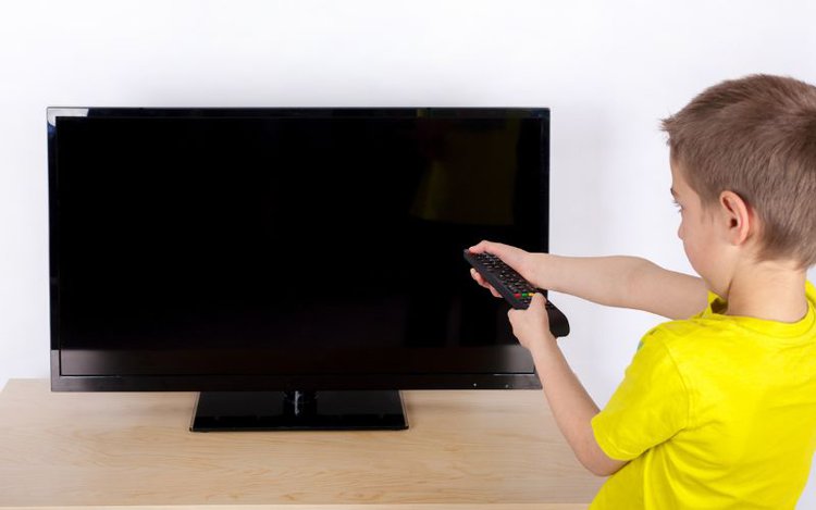 a boy tries to turn on the TV with remote but it does not work