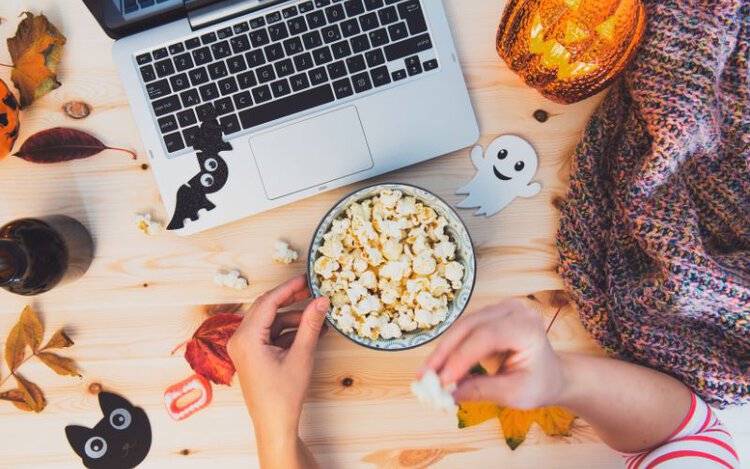 a person eating popcorn while watching movies on laptop