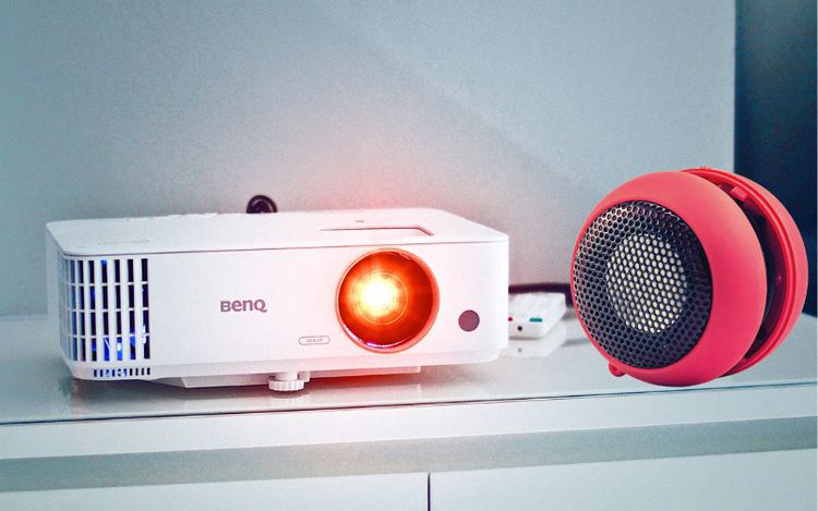 a red speaker lying next to the BenQ projector