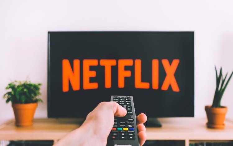 hand holding a remote towards a TV with Netflix logo on