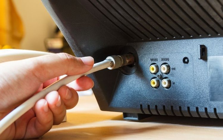 hand holding a white TV aerial cable plugged in the back of TV