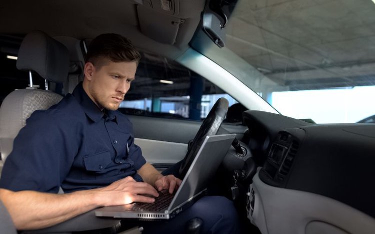 male officer working on laptop in his car about the TV licence