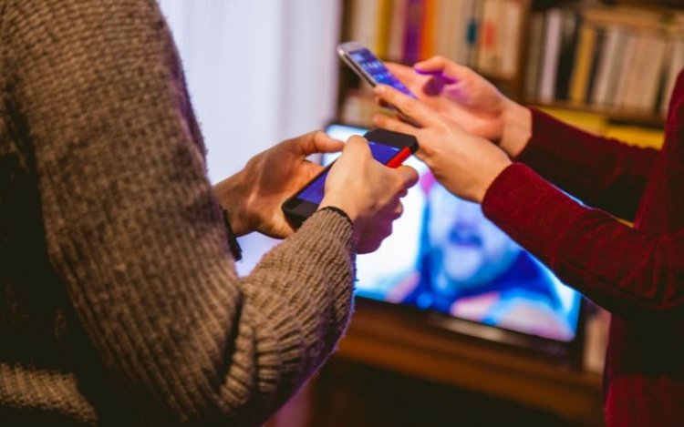 man and woman are playing with their phone when watching tv