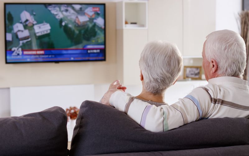 old couple watching TV hanging on the wall at home