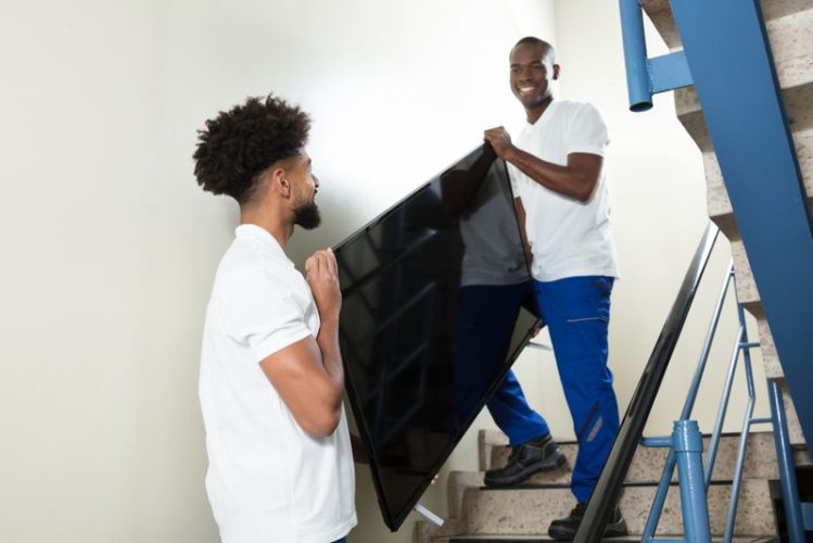 two young man carrying a TV down the stairs