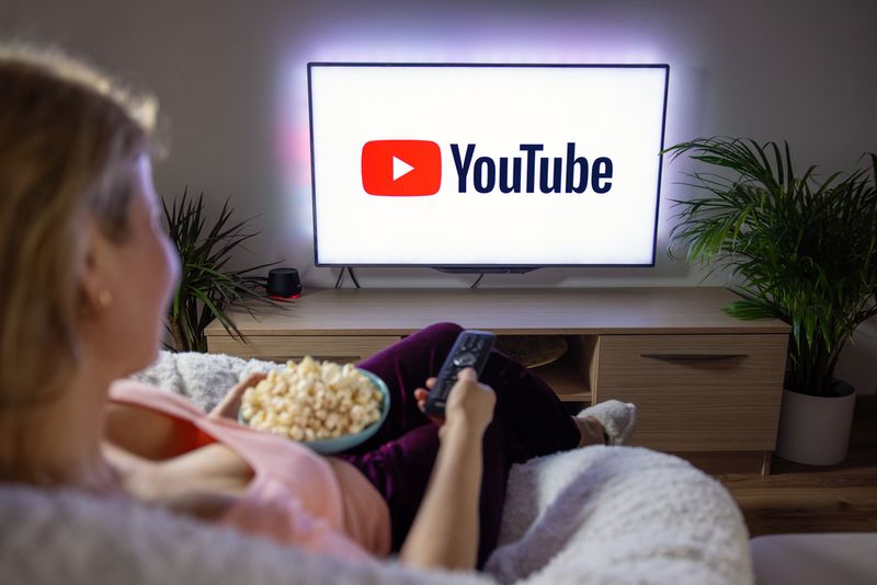 woman holding popcorn and watching TV with YouTube logo on the screen