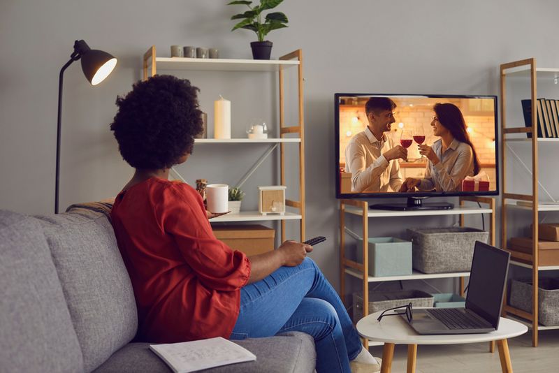 woman watching TV with a couple drinking wine on the screen in living room