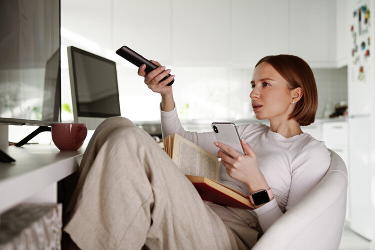 A woman is reading book and watching tv at the same time 