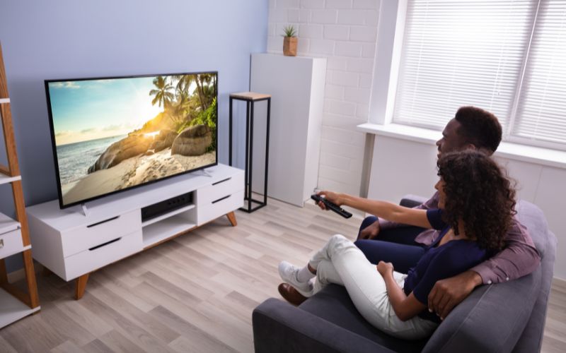 a couple is watching TV on a bright room with sun blinds