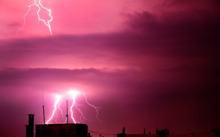 lightning strikes over the roof of houses