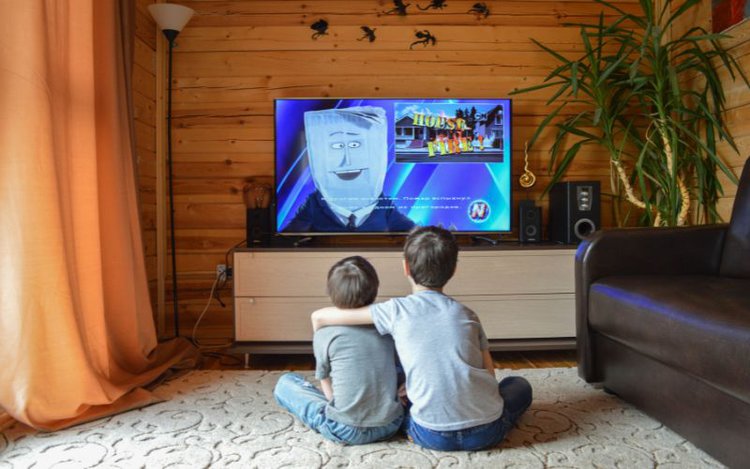 two kids enjoy watching cartoon on TV in a bright room with curtains