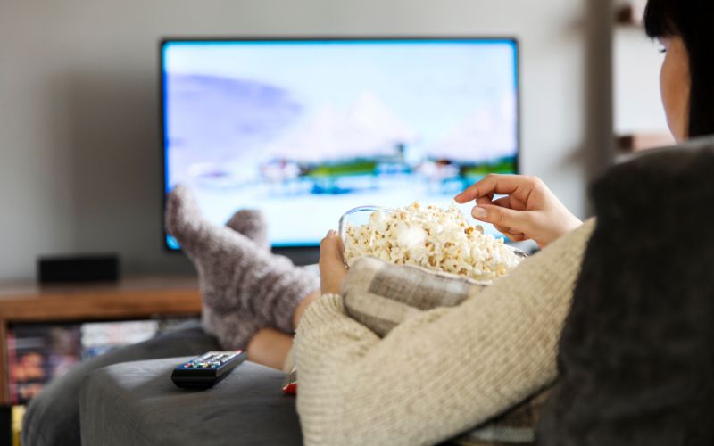 woman enjoys watching TV with popcorn while on sofa