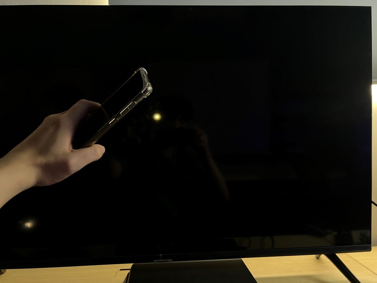 A hand is holding a phone and shine flash light to a Samsung TV