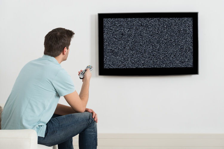 A man sit in front of a losing signal TV