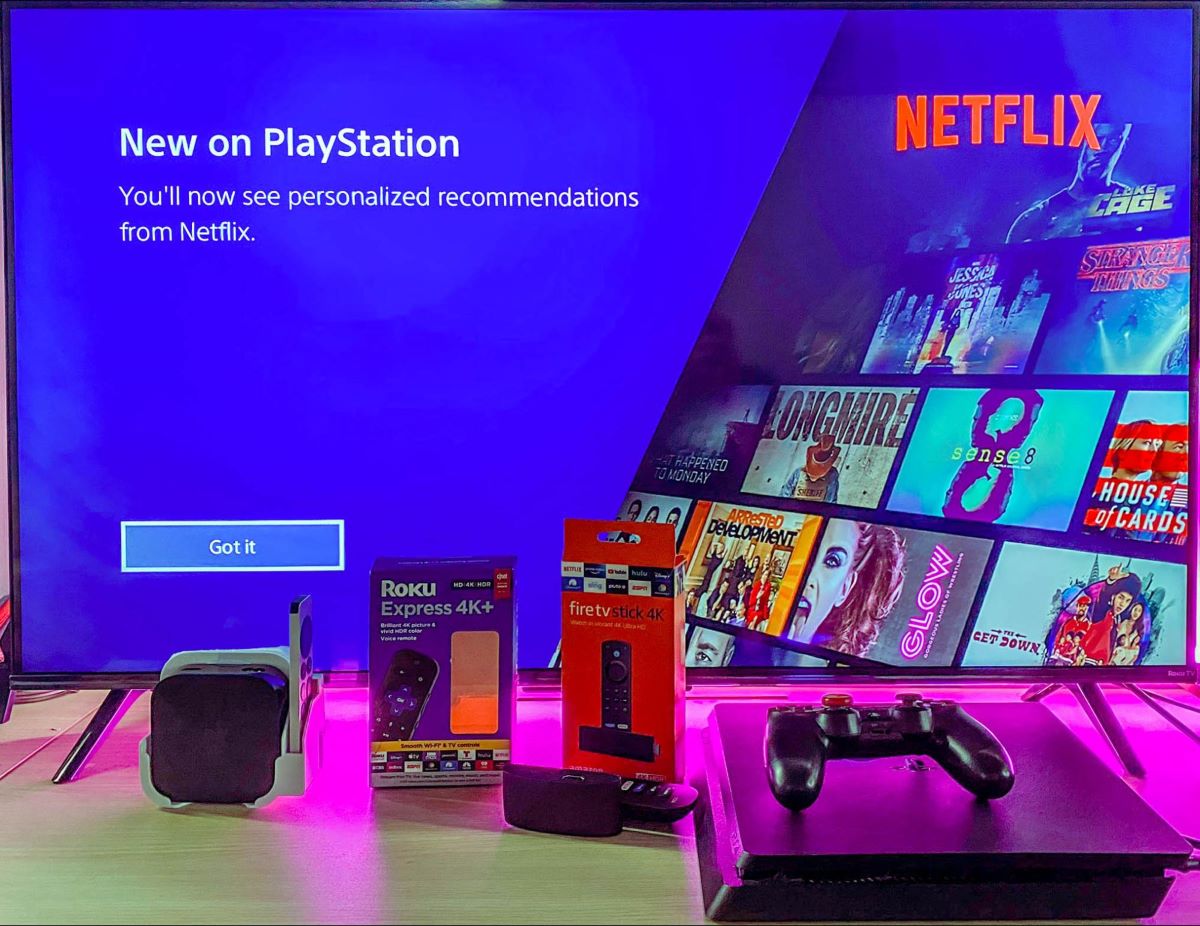 Roku, Firestick, Apple TV box, and a PS4 are placed in front of a TV while showing Netflix via PlayStation service