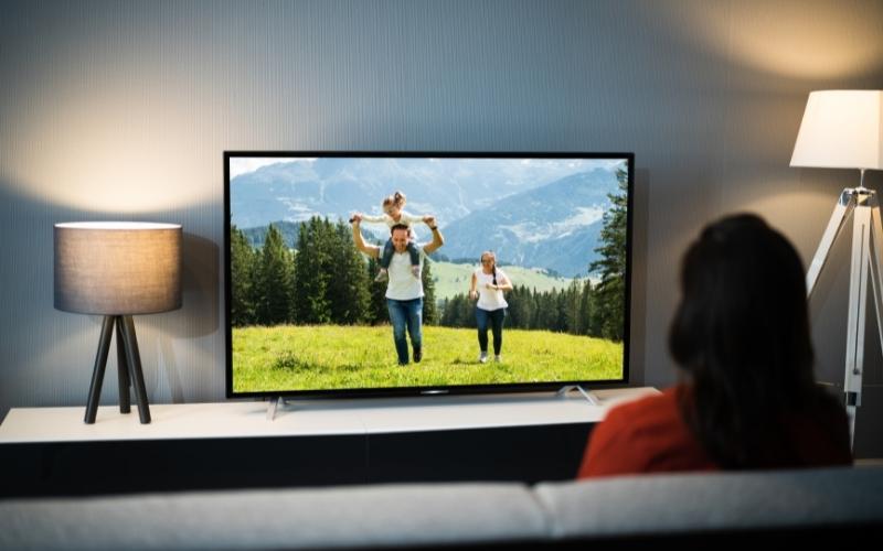 a woman watches a happy family on TV