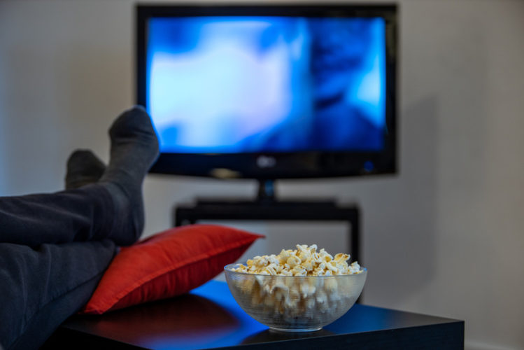 man watching a blurry TV with foot over the table and bowl of popcorn