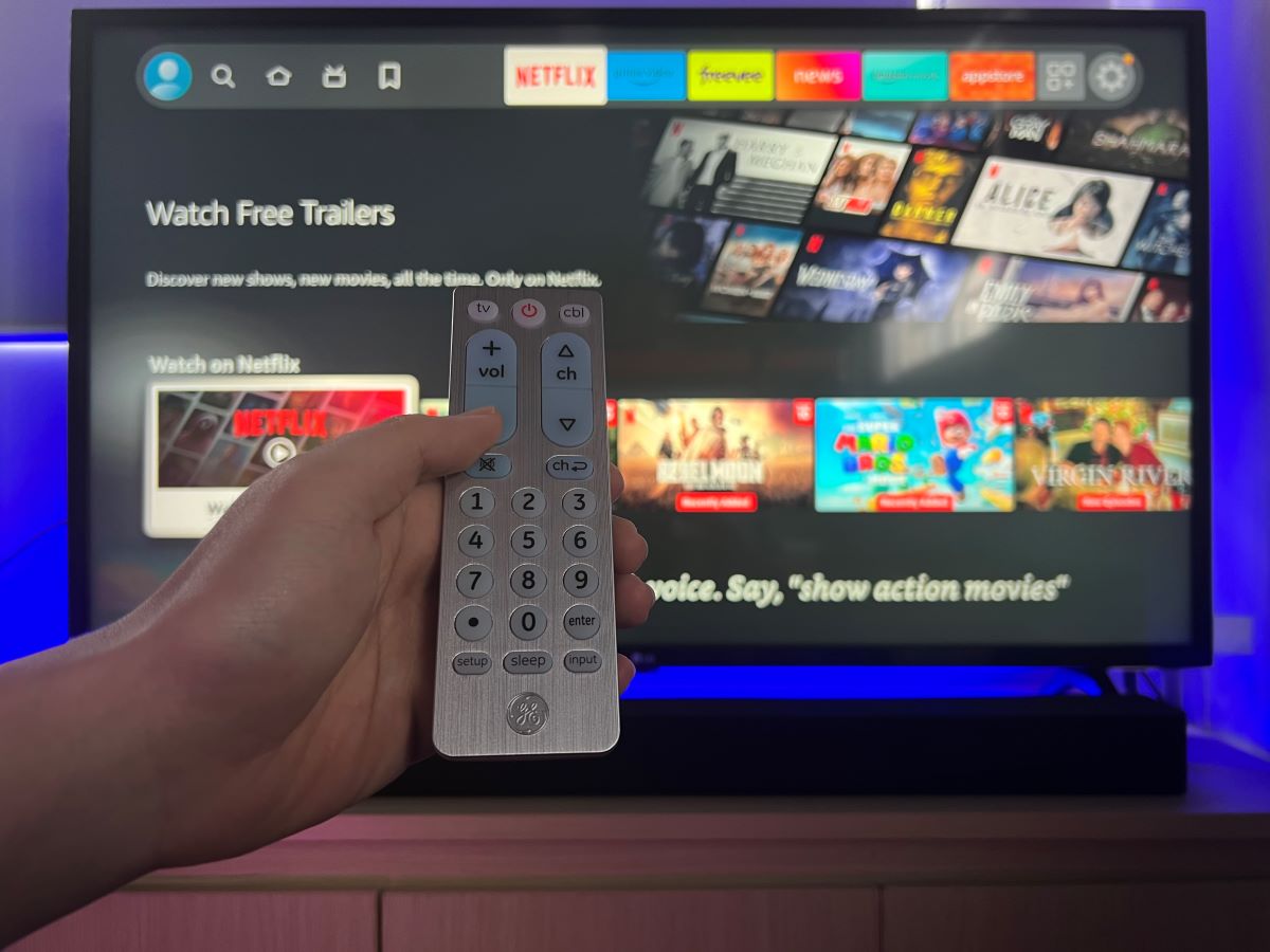 A hand is hlding the GE remote control and try to control the Fire TV