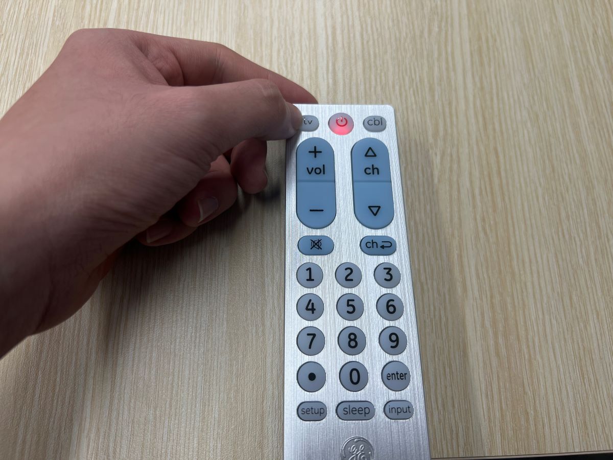 A hand is hold the pairing button on GE universal remote