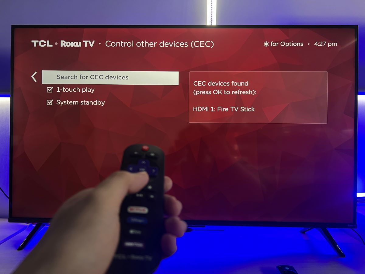 A hand is holding a remote and control the TCL Roku TV