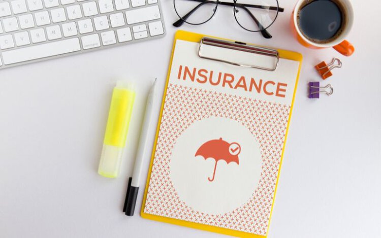 insurance paper on yellow clipboard with keyboard, pens, glasses and cup of coffee