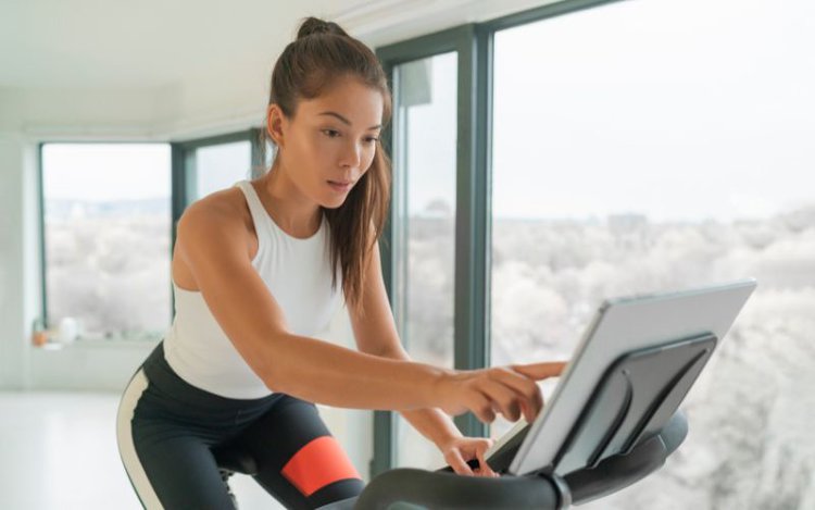 woman doing her home cycling workout and clicking on the bike's touchscreen