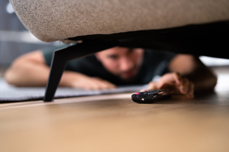 A man find a remote under the sofa