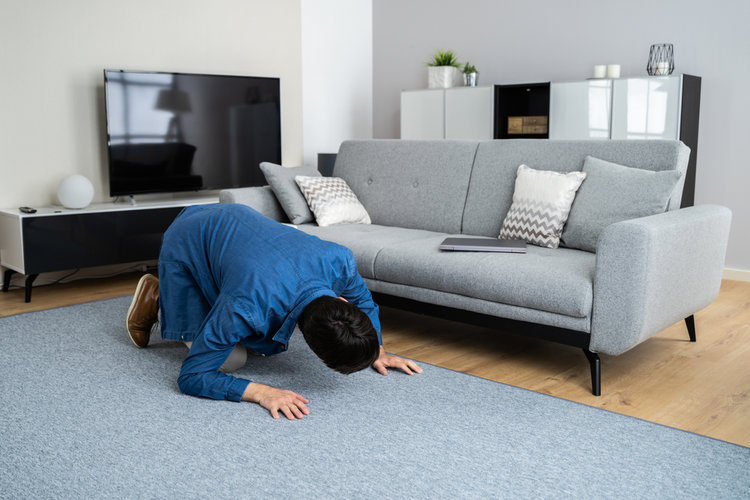 A man searching under a sofa in the living room