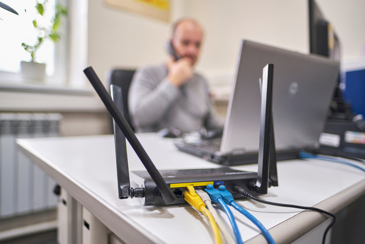 Wifi router on the edge of table with plugged in cables and man working in the background