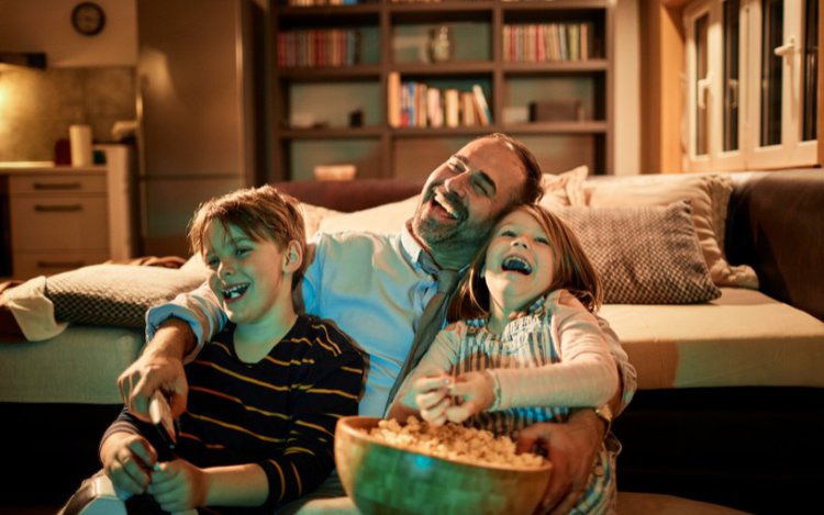 a father with his son and daughter laugh when watching TV