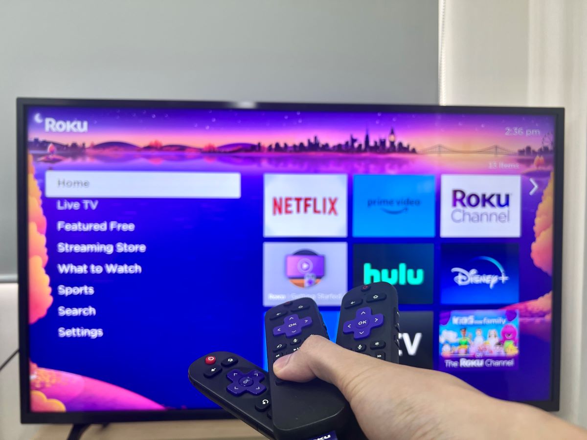 a hand holding three roku remotes pointing at a tv