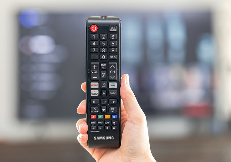 hand holding a Samsung TV remote in front of blur TV background