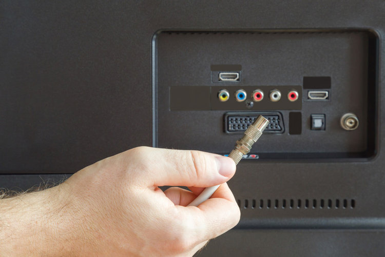 man holding a coaxial cable in front of the back view of TV