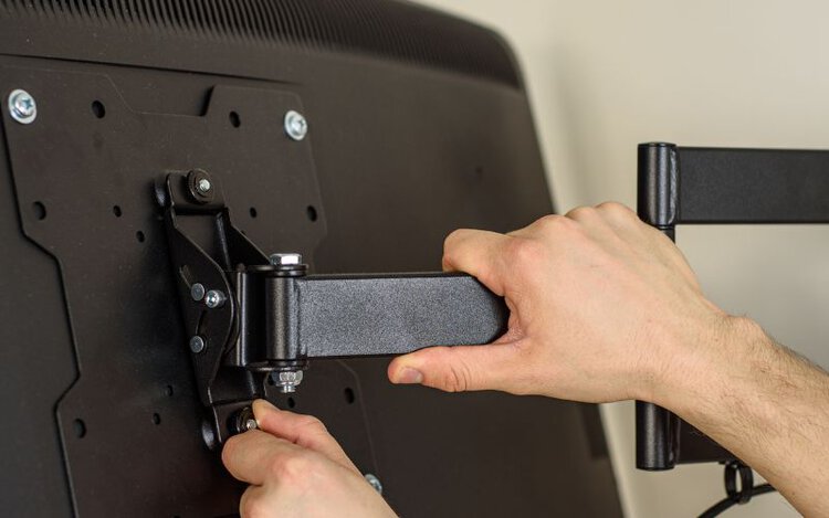 man is screwing the wall mount bracket with the back of TV