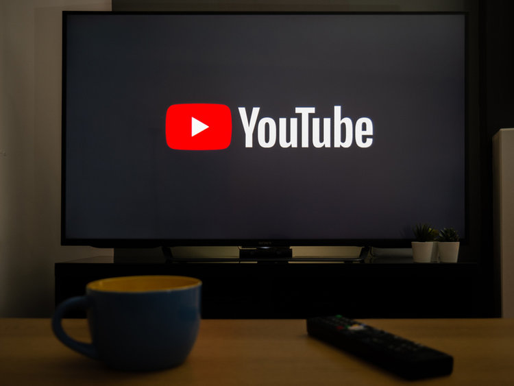 a TV behind a cup and remote with YouTube logo on screen