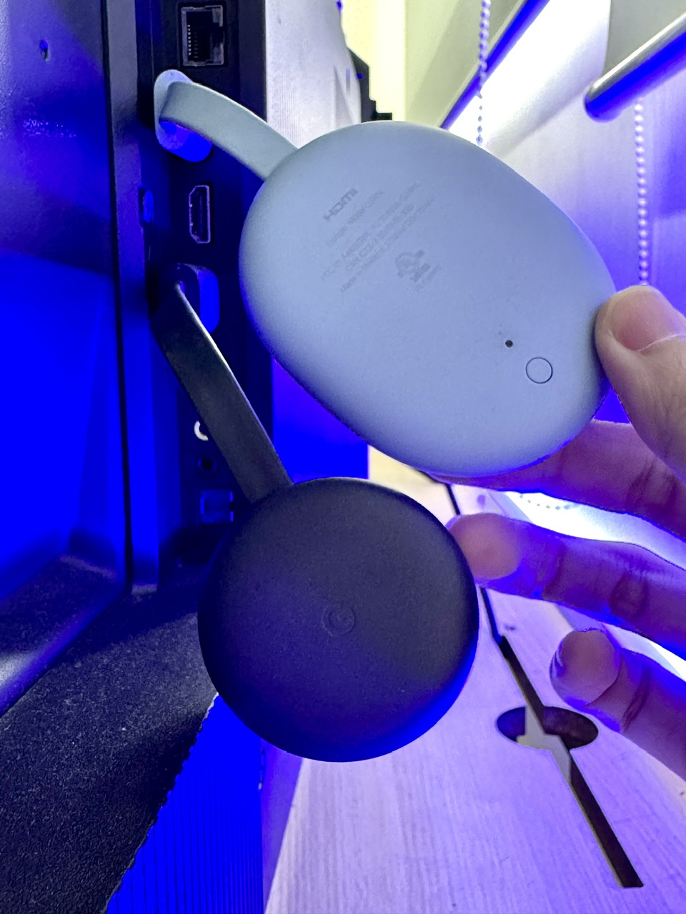 a hand holding a chromecast with google tv right above a chromecast without google tv, both plugged into the tcl tv