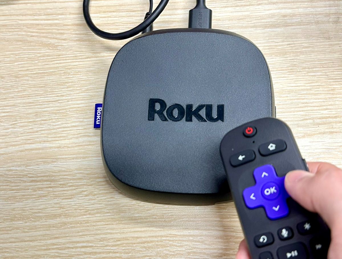 a hand holding a roku remote in front of a roku ultra