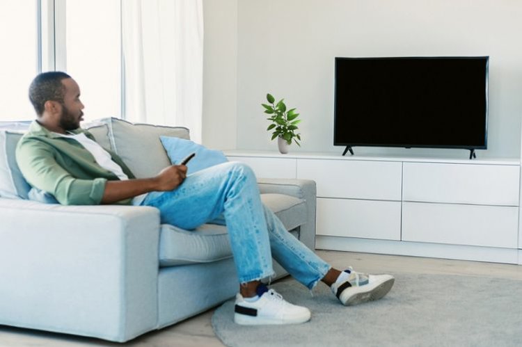 young black man holds TV remote and look at TV screen