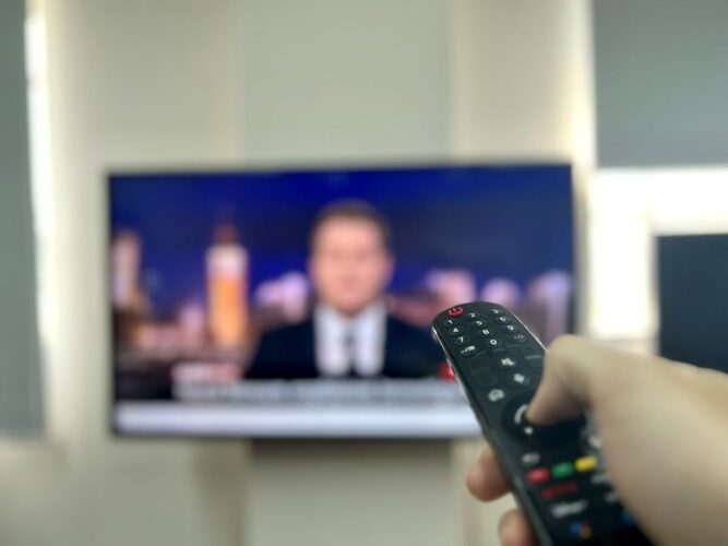 a hand holding an lg remote with an lg tv blurred in the background