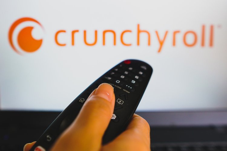hand holding TV remote in front of Crunchyroll logo