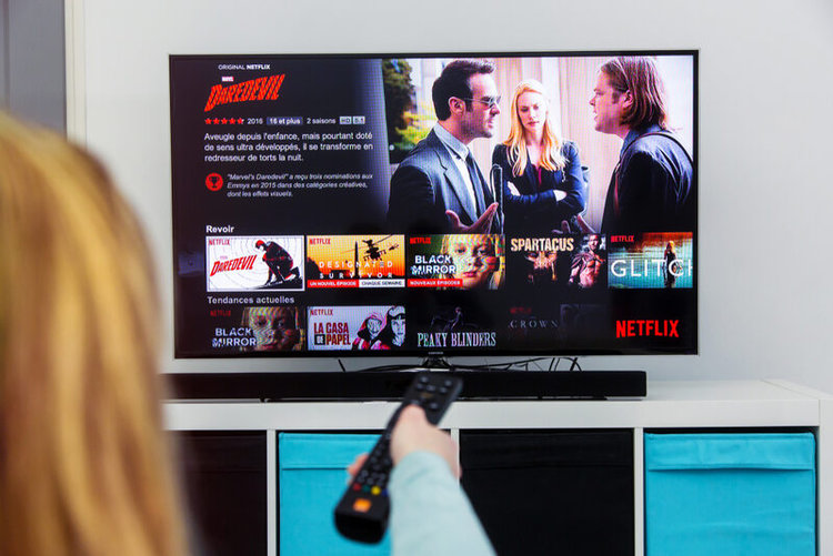 woman pointing the remote towards a TV with Netflix app on the screen