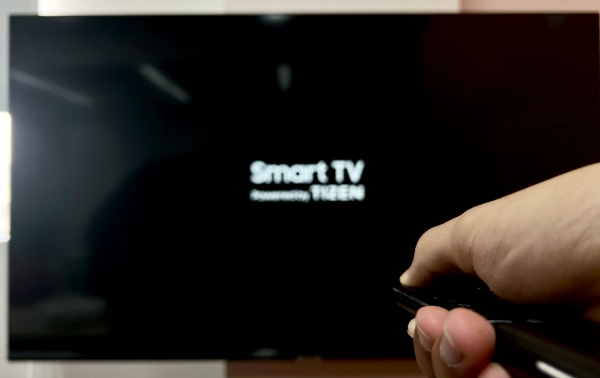 hand pressing the Power button on remote in front of blurr Smart TV