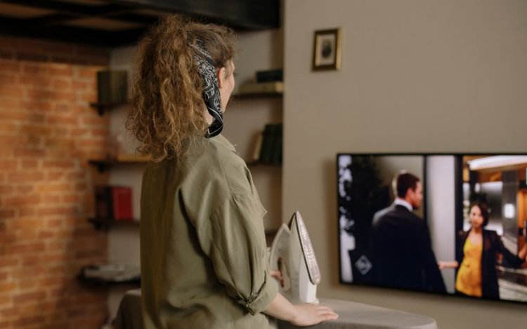 woman watching tv while standing to iron her clothes