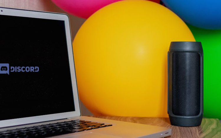 laptop with colorful balloons around connected to a bluetooth speaker accesses to discord web