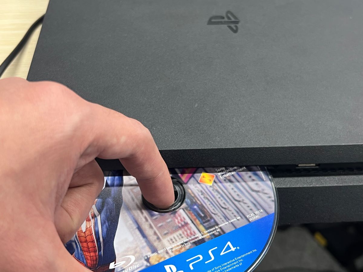 A hand is removing the Spider-Man disc game on the PS4 console safely
