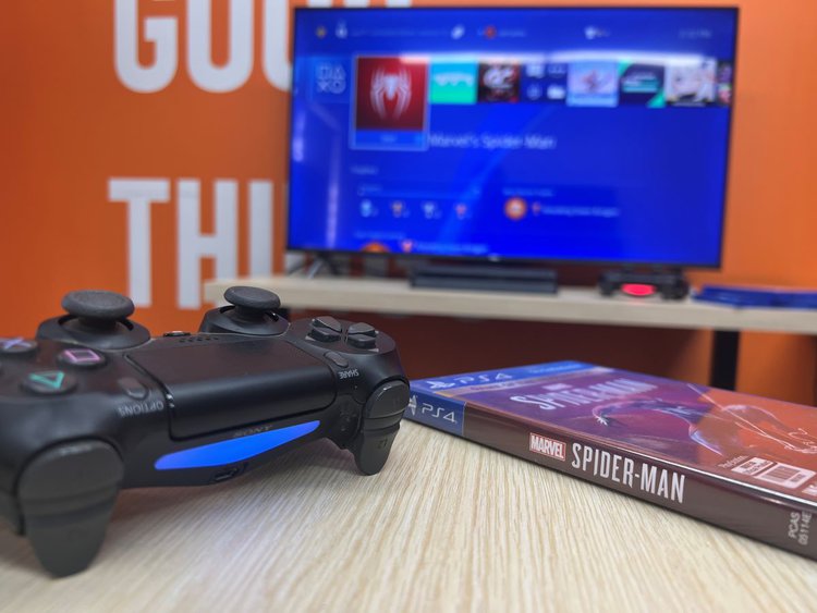 PS4 controller and spider-man game with TV at the back
