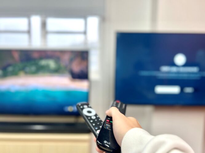 a hand holding 2 remotes pointing at the spot between two tvs