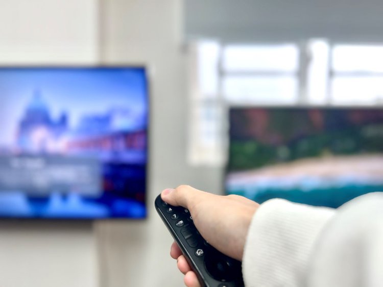 a hand holding a remote pointing at the spot between two tvs